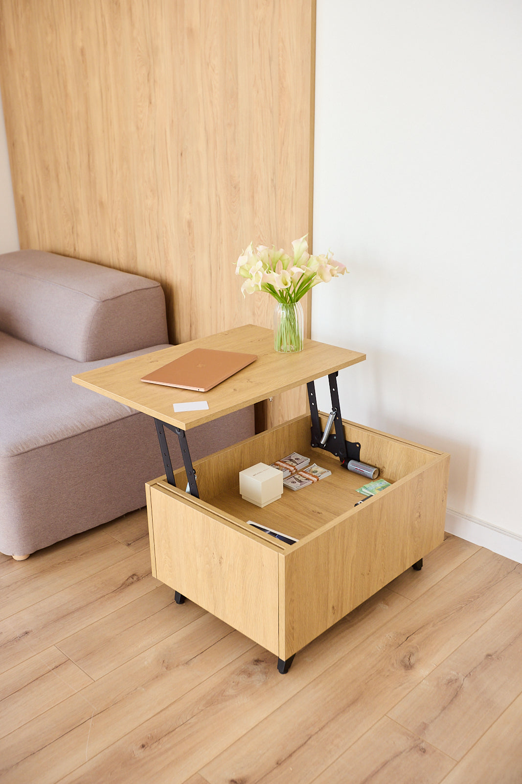 A light wood rolling storage ottoman table with a lift-up top and open storage compartment below, shown in a modern living room setting next to a sofa