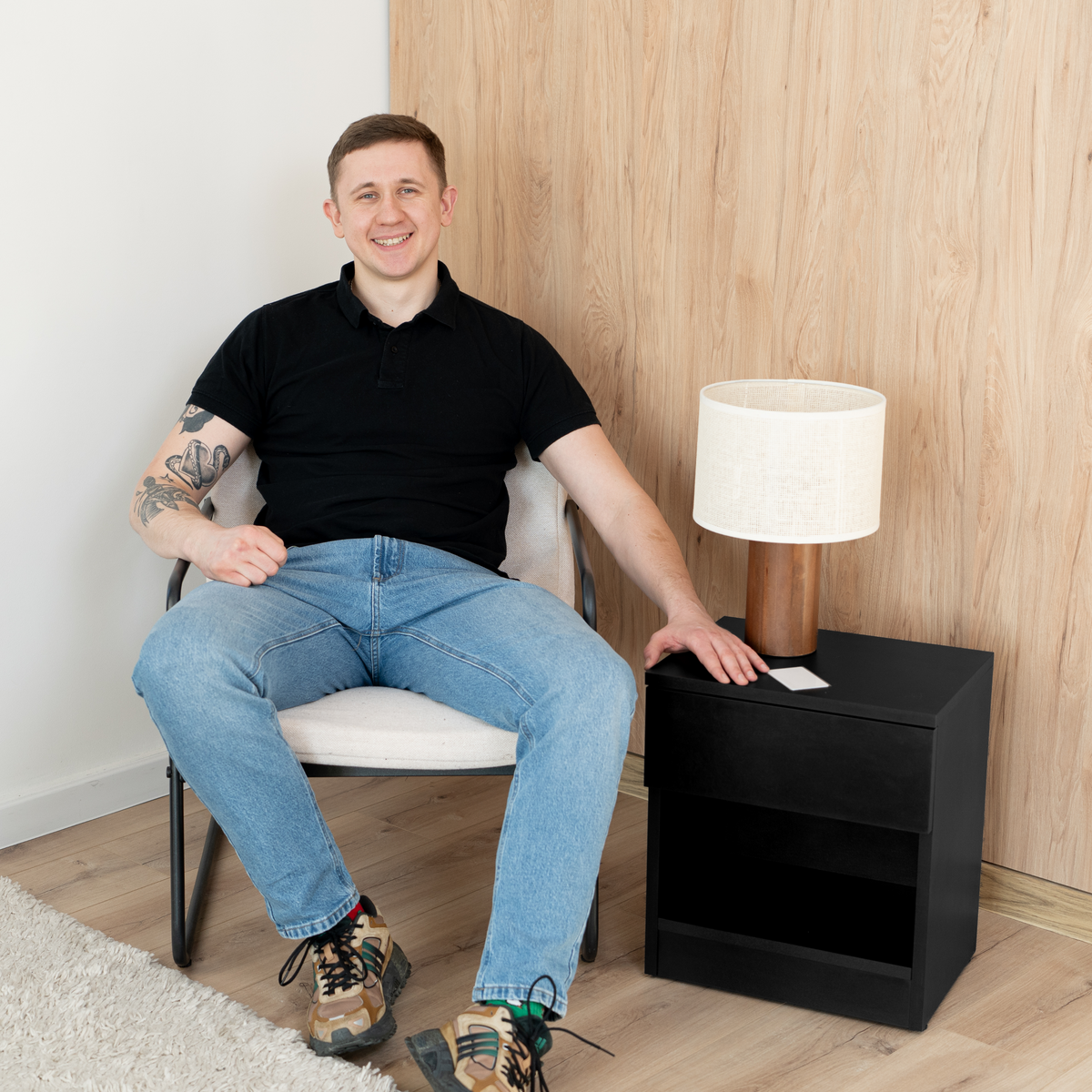 Person sitting beside a modern black nightstand and lamp