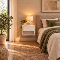 A modern bedroom scene featuring a white floating nightstand with a lit table lamp and a small potted plant, next to a bed with beige bedding and a textured green throw blanket.