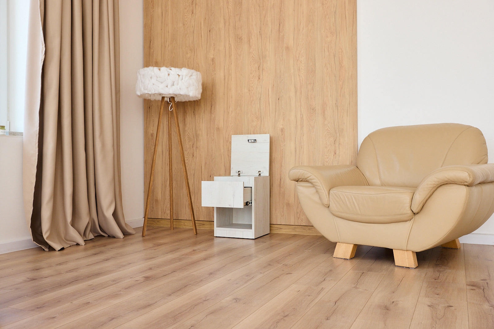 A beige leather armchair in a modern living room with light wood flooring, a wood-paneled wall, a floor lamp, and a small white bedside table with hidden compartment
