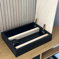 Hidden Wall Storage with Contactless RFID Lock. A black wooden storage box with its lid raised, showing the hinge hardware and light wood interior supports, placed on a wooden table against a paneled wall.