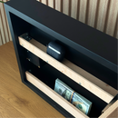 Modern Wave Wall Art with Concealed Storage. A black and wood safe or storage cabinet shown open, with a stack of cash in the lower compartment and a small round black device resting on a wooden shelf.