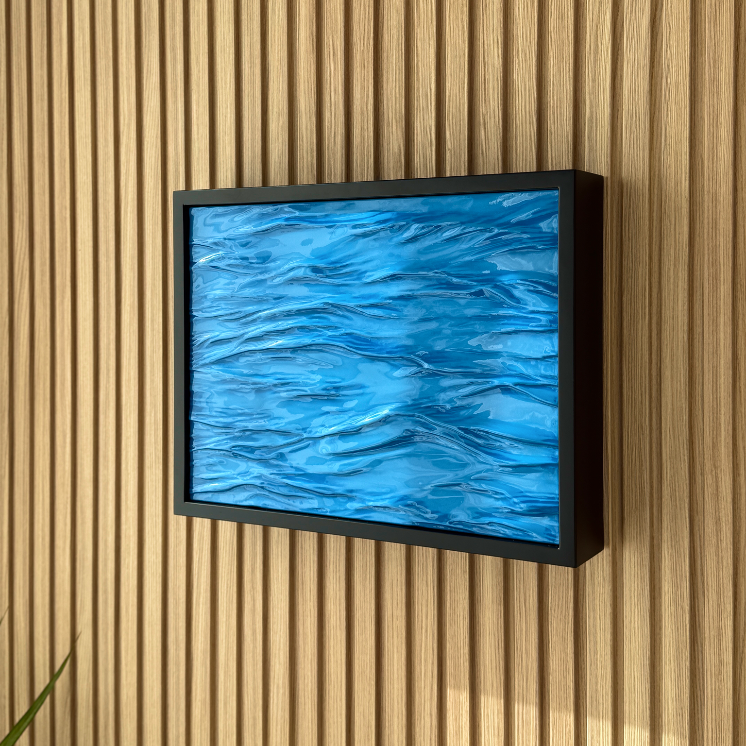 Modern Wave Wall Art with Concealed Storage. A framed wall art piece featuring a textured blue abstract water-like pattern, mounted on a light wood slatted wall.