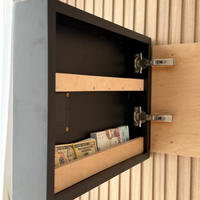 Wave Wall Art with Hidden RFID Storage Compartmentю A black wall-mounted safe or storage cabinet shown open, with wooden interior shelves and cash stored inside, set against a light wood slatted wall.