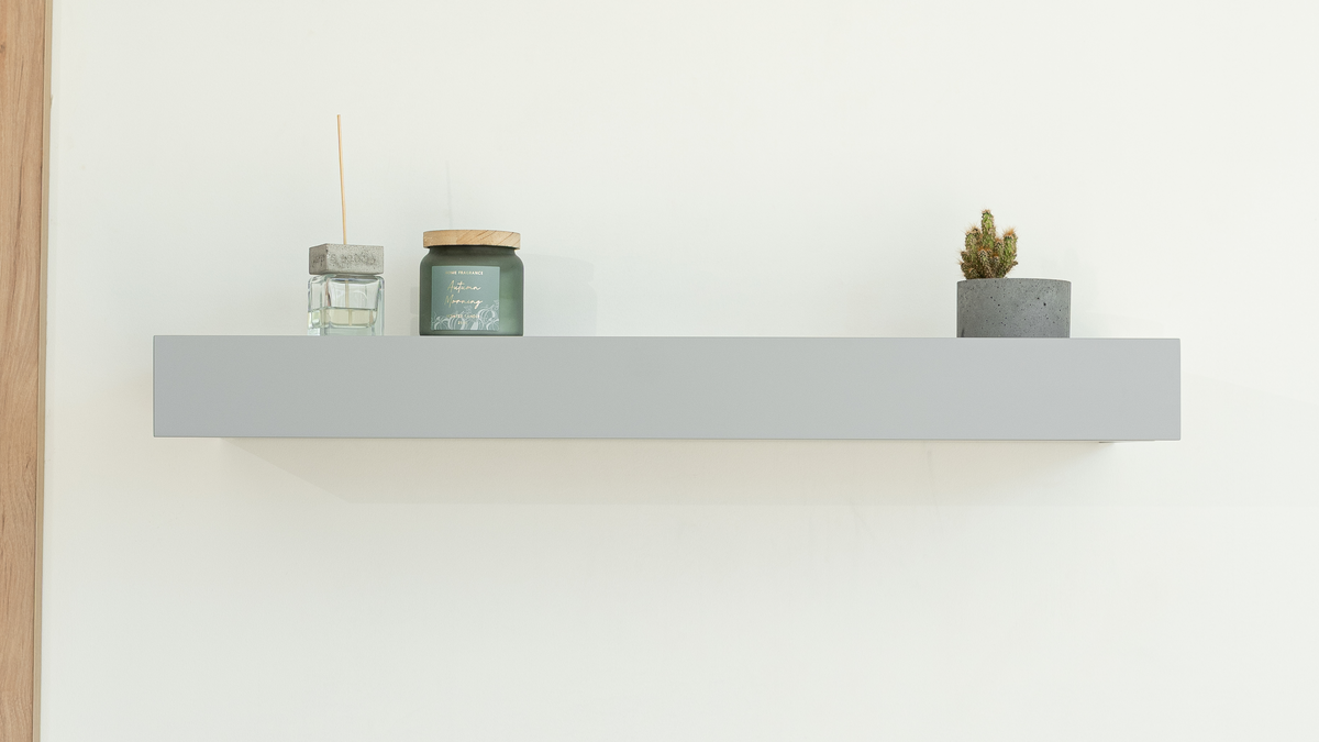 Closed grey floating shelf with decorative items on a white wall